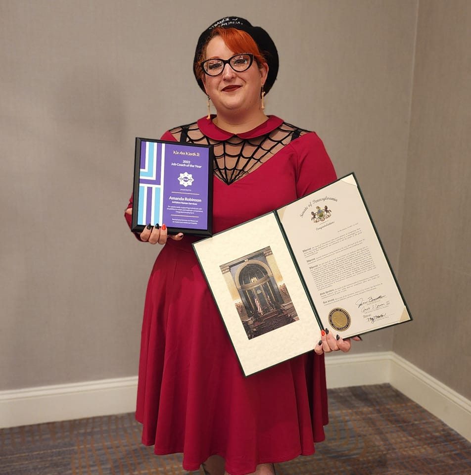 Amanda Robinson standing proudly while displaying official We Are Worth It award against a beige wall