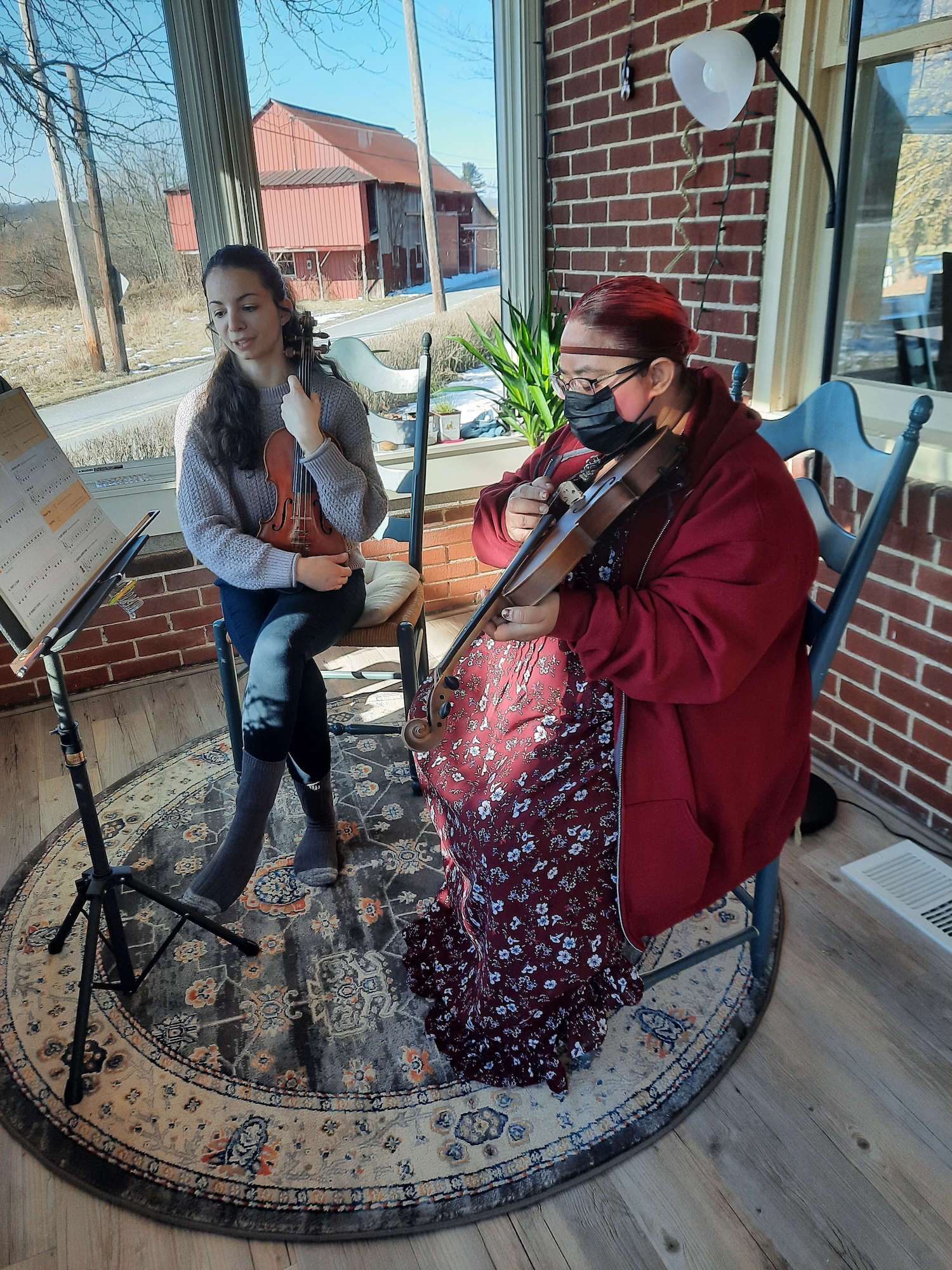 two women sitting on a residential home front porch practicing violin