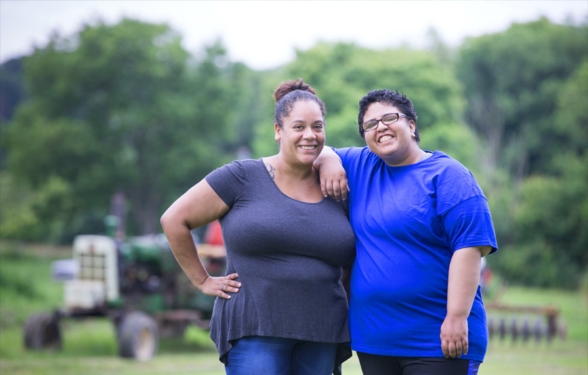 woman dsp and woman person supported in open field by a farm tractor smiling posed with one arm each around the other